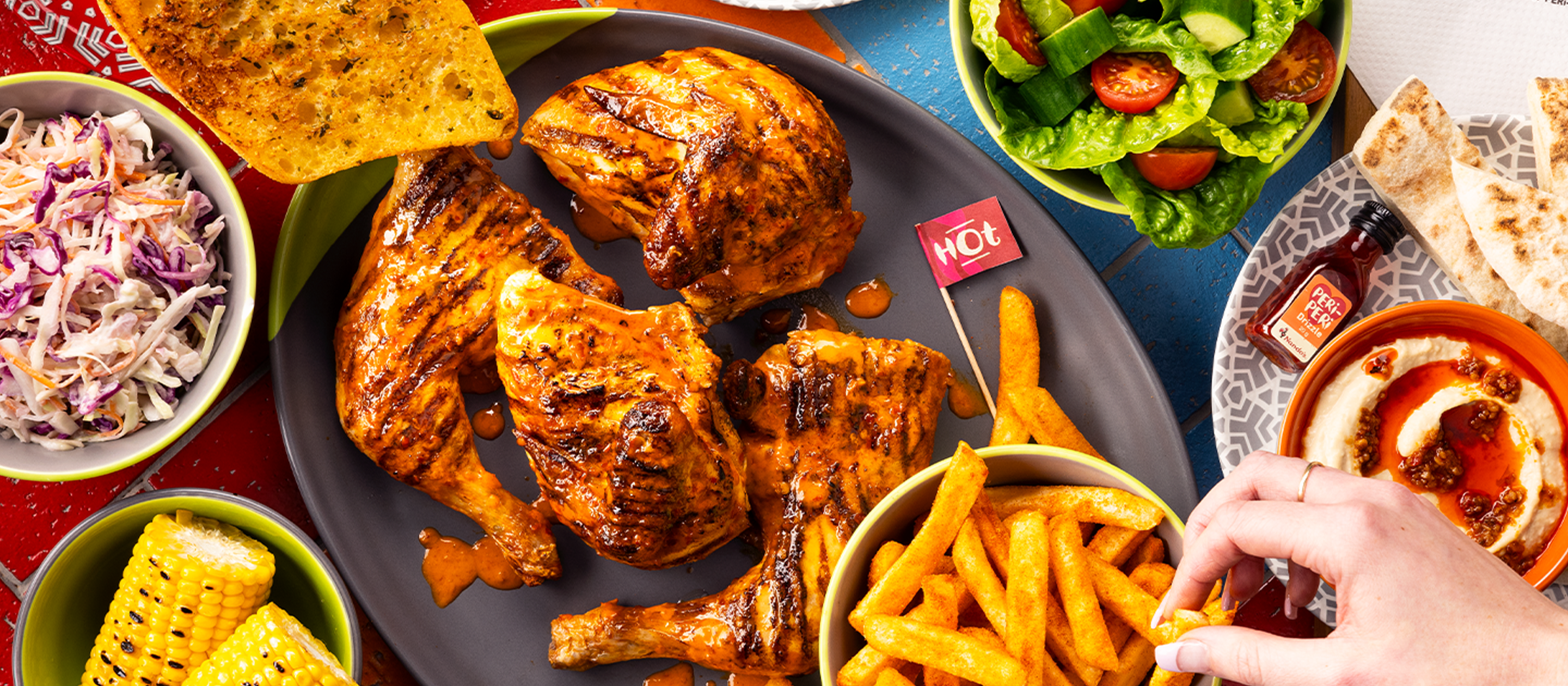 a Nando’s meal on a table including PERi-PERi chicken, a salad, chips, and a selection of sides