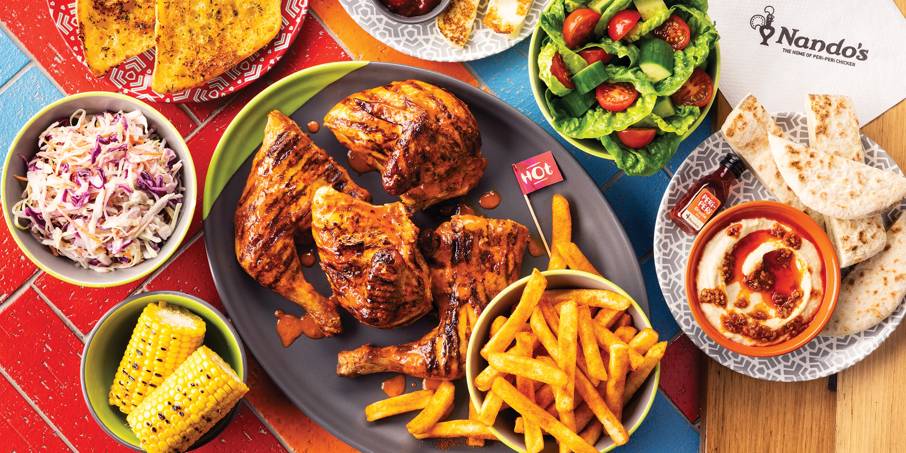 a Nando’s meal on a table including PERi-PERi chicken, a salad, chips, and a selection of sides